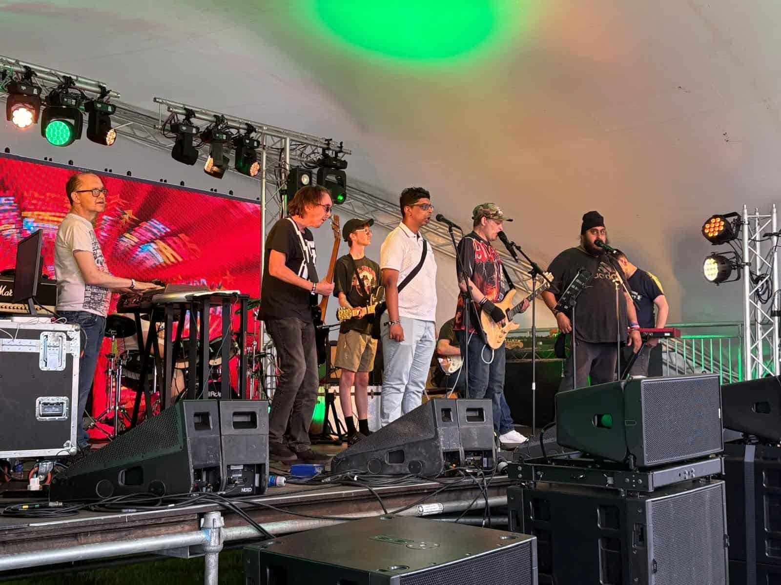The Under the Stars band performing live on stage at Tramlines, with musicians and singers performing together under colourful stage lighting.
