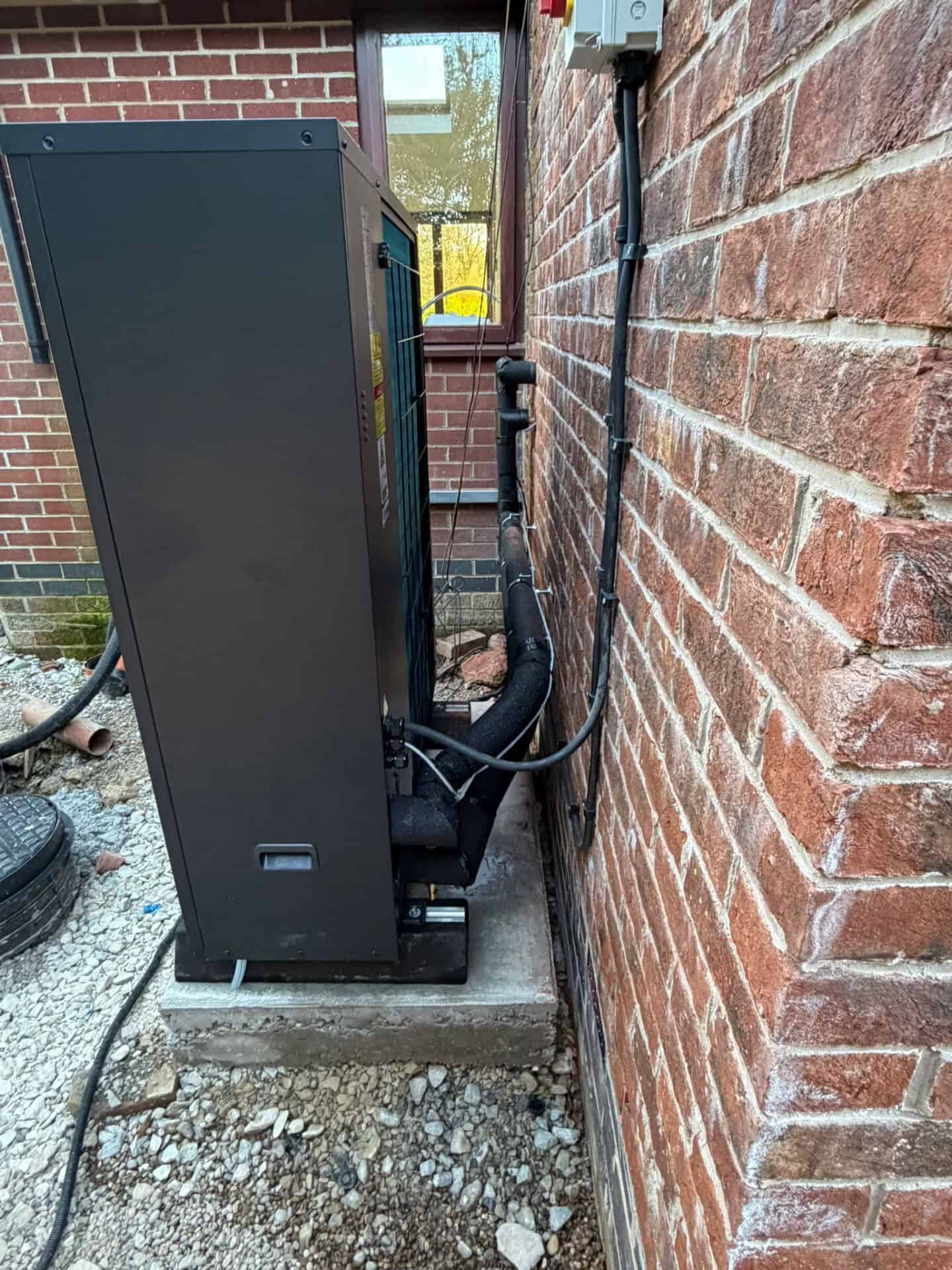 Side view of a Grant Aerona air source heat pump showing insulated pipework connected to the property.
