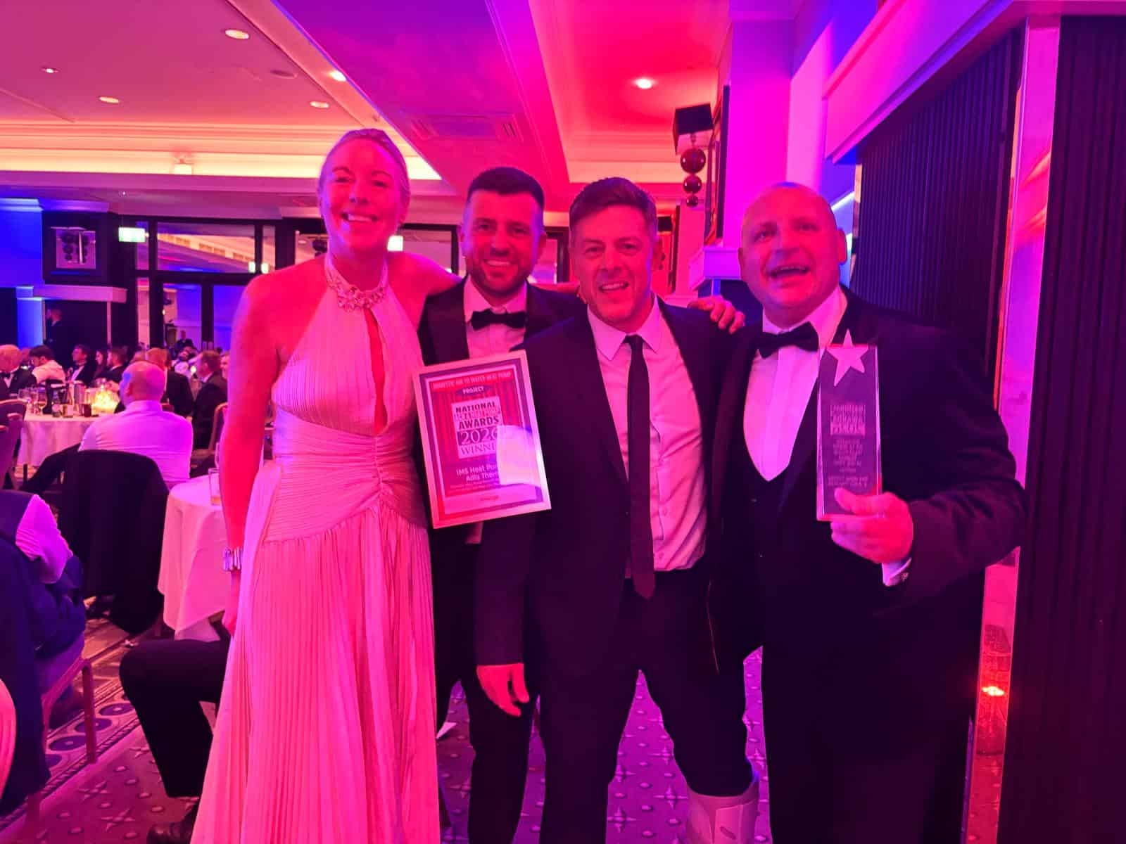 Emma Bohan, Managing Director of IMS Heat Pumps, stands with Christian Holmes, Heating Engineer, Lee Brown, Operations Director, and Dave Lakin, Senior Heating Engineer, at the National ACR & Heat Pump Awards 2026. Dressed in formal evening wear, the team are smiling and celebrating after winning Domestic Air to Water Heat Pump Project of the Year, proudly displaying their winner's certificate and trophy. The awards ceremony takes place in a brightly lit ballroom with fellow industry guests seated in the background.