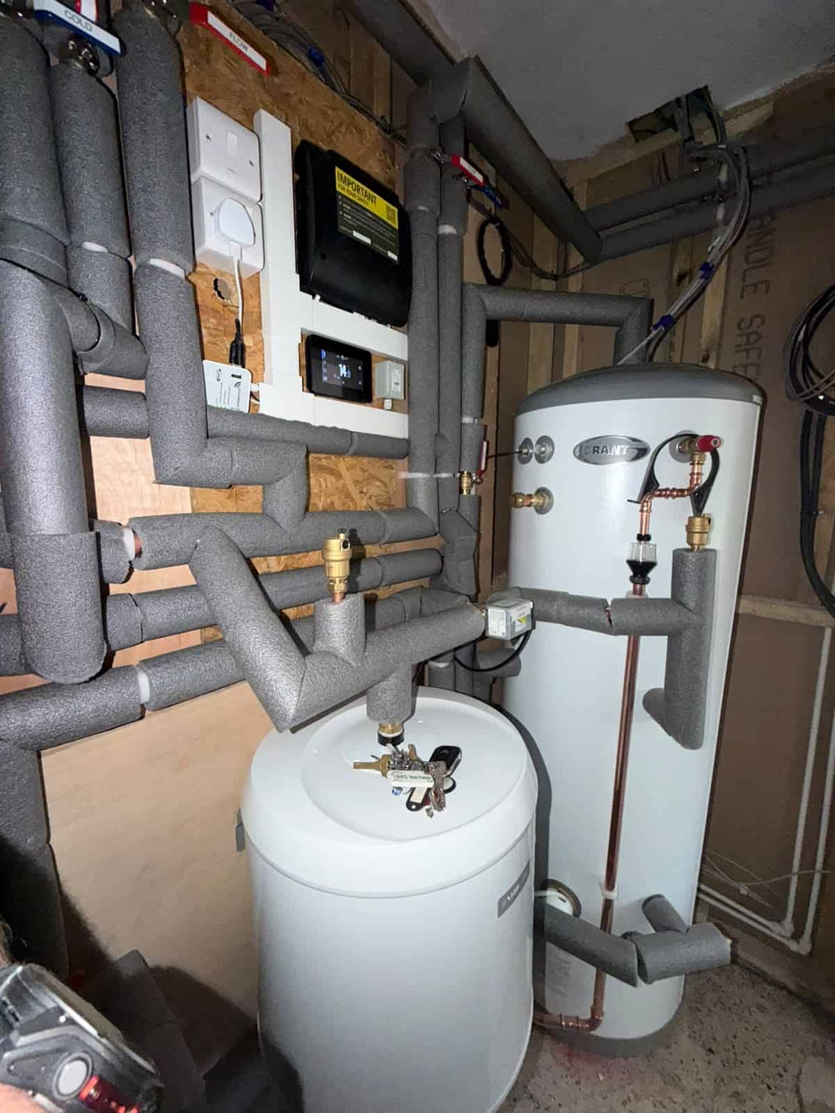 Neatly installed air source heat pump plant room with insulated pipework, controls, buffer vessel and expansion vessels.